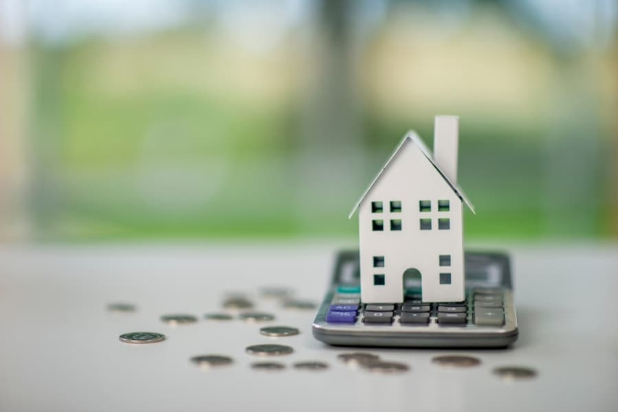 Small white house model resting on scattered coins