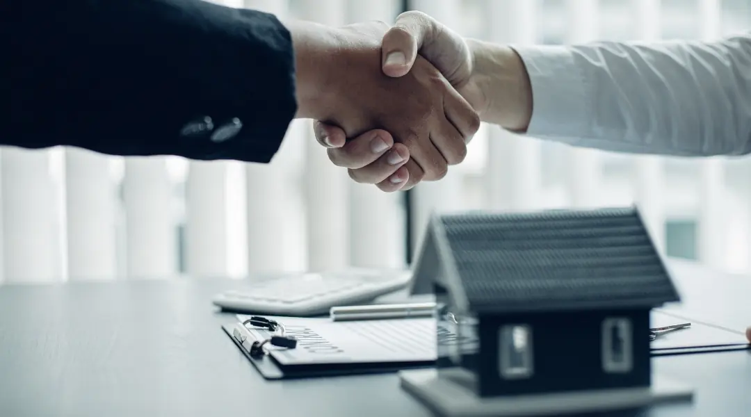 A homebuyer and advisor shaking hands beside a model home