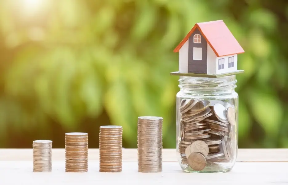 A model home above a jar of coins and savings